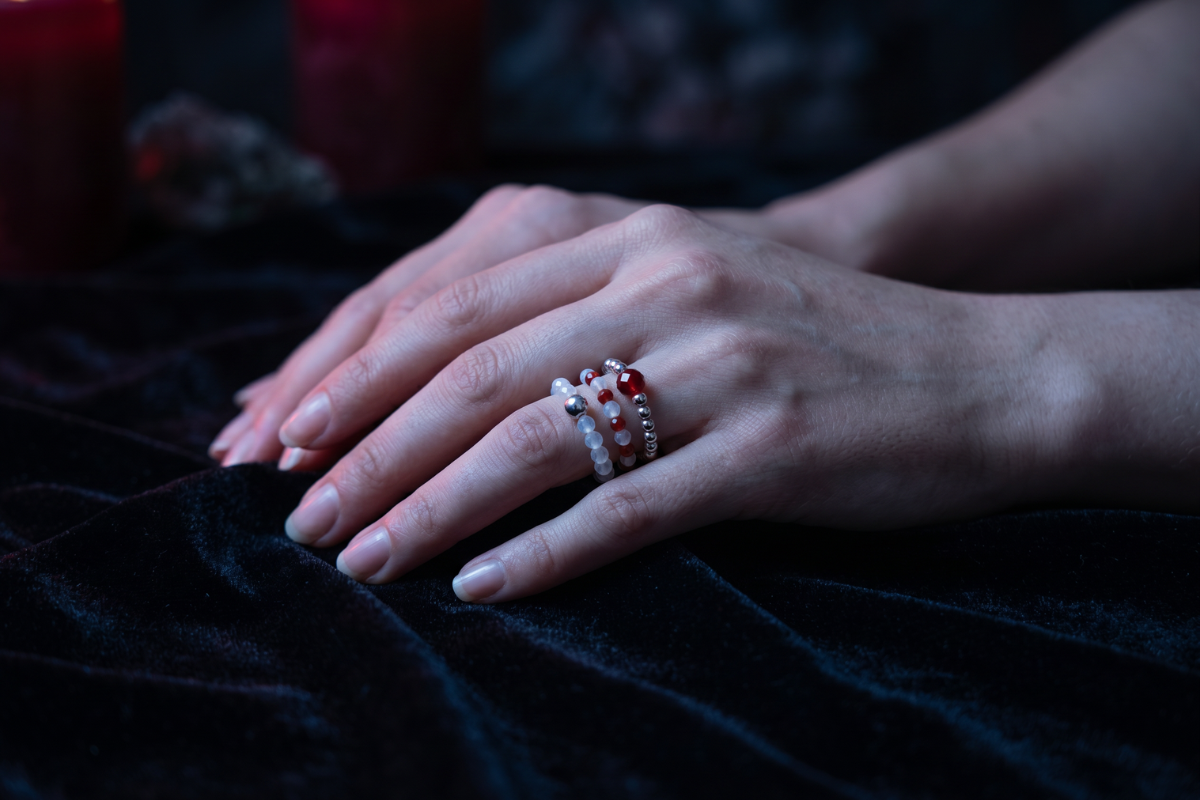 Tre l�se 'Blood Moon' elastikringe lagt samlet. Ringene best�r af dybr�d rubin, lysende hvid m�nesten og sm�, blanke fors�lvede perler.