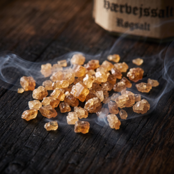 Makrobillede af rav-farvede, r�gfyldte saltkrystaller, der ligger p� m�rkt, rustikt egetr� indhyllet i bl�d hvid r�g.