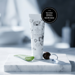 Flowus CBD ansigtscreme pr�senteret p� hvidt marmor omgivet af en frisk aloevera-blomst og en eksotisk kukui-n�d.