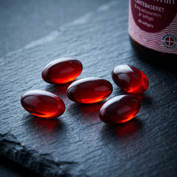 Et ekstremt n�rbillede af skinnende, dybr�de veganske softgels, der ligger p� en m�rk og rustik stenoverflade badet i dramatisk, k�ligt lys.