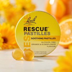 Et krystalklart makrobillede af to perfekt afrundede, gyldne og let transparente Rescue-pastiller placeret sirligt p� en ren overflade foran den realistiske, gule Bach Rescue metald�se (helt uden pipetter eller v�skedr�ber). Den bl�dt sl�rede baggrund kombinerer str�lende morgenfrue-gule (marigold) nuancer og lette orange/solrige refleksioner fra et vindue, som diskret og elegant repr�senterer den friske appelsin/hyldeblomst smag og de botaniske essenser. Lyset er varmt, lyst og indbydende, hvilket fremh�ver total f�devarekvalitet og renhed. Knivskarpt fokus.