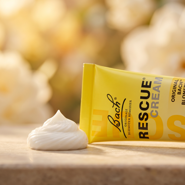 Et krystalklart makrobillede af en perfekt, struktureret klat af rig, n�rende hvid creme med sheasm�r, placeret sirligt p� en ren overflade ved siden af den realistiske, ikoniske gule Bach Rescue Creme tube (helt uden pipetter, dr�bet�llere eller v�ske). Den bl�dt sl�rede baggrund kombinerer lyse, bl�de cremehvide nuancer, varme gyldne og gule toner fra sollys, som diskret og elegant repr�senterer den botaniske renhed fra Dr. Bachs blomsteressenser. Lyset er ekstremt varmt, bl�dt og indbydende, hvilket fremh�ver total kosmetisk renhed uden at virke for sterilt. Knivskarpt fokus.