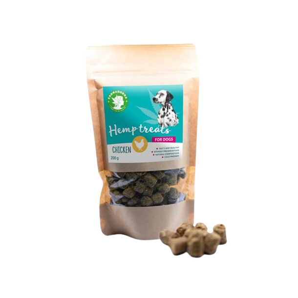 En papirspose med Cannadorra Premium Hundegodbidder med Hamp og kylling. Etiketten er turkis og viser et billede af en dalmatiner og et lille gult kyllingesymbol. Flere m�rke, koldpressede godbidder ligger foran posen.
