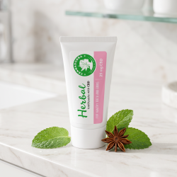 N�rbillede af den hvide, gr�nne og lyser�de Cannadorra CBD tandpasta tube, der st�r skarpt p� en lys badev�relseshylde. Friske gr�nne mynteblade og hele stjerneanis ligger dekorativt omkring tuben i et rent dagslys.