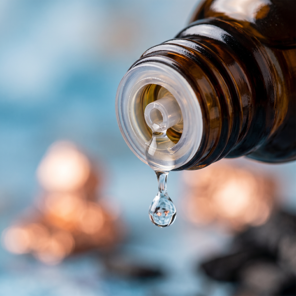 Et krystalklart makrobillede af en vanddr�be, der falder fra den indbyggede dr�bet�ller p� en m�rk ravfarvet glasflaske. Den bl�dt sl�rede baggrund kombinerer svale, friske bl� nuancer med varme, gyldne strejf af metallisk kobber (Cuprum) og m�rke antydninger af birkekul. Lyset er klart, opkvikkende og beroligende p� samme tid.
