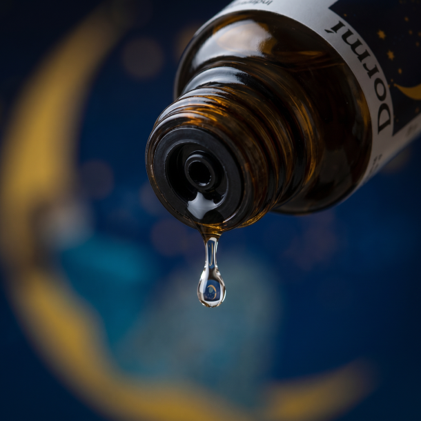 Et krystalklart makrobillede af en vanddr�be, der falder fra den indbyggede dr�bet�ller p� en m�rk ravfarvet glasflaske. Den bl�dt sl�rede baggrund kombinerer dybe, m�rke nattebl� nuancer med blide strejf af lysende, varm m�negul (Phosphorus). Lyset er svalt, d�mpet og udstr�ler absolut nattero og afsp�nding.