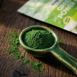 N�rbillede af et fyldigt, m�rkegr�nt plantepulver af spirulina, chlorella og hvedegr�s anrettet smukt i en h�ndlavet keramikske p� en rustik tr�baggrund.