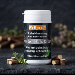 N�rbillede af den hvide og sorte Fribol Lakrids d�se, st�ende skarpt p� en m�rkegr� stenplade. Sm� stykker af r� lakridsrod og en enkelt kvist frisk, gr�n timian ligger smukt spredt foran d�sen i et bl�dt lys.