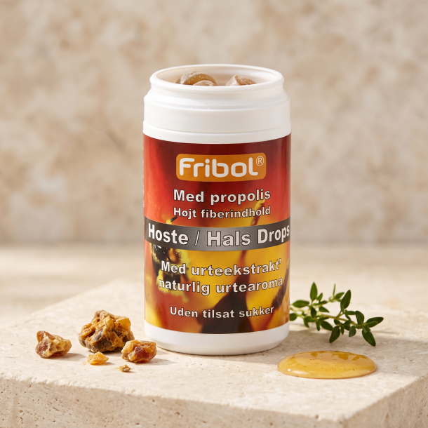 N�rbillede af den hvide og ravgyldne Fribol Propolis d�se, st�ende skarpt p� en lys stenplade. Sm�, gyldne stykker af propolis, en kvist gr�n timian og en dryp af karamel/honning ligger smukt spredt foran d�sen i et varmt, indbydende lys.