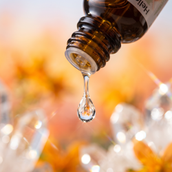 Et krystalklart makrobillede af en vanddr�be, der falder fra den indbyggede dr�bet�ller p� en m�rk ravfarvet glasflaske. Den bl�dt sl�rede baggrund kombinerer varme, solrige orange og blide ferskenfarvede nuancer, blandet med lysende krystallinske glimt fra kisel (Quartz). Lyset er utroligt klart, opl�ftende og udstr�ler absolut harmoni og indre solskin.