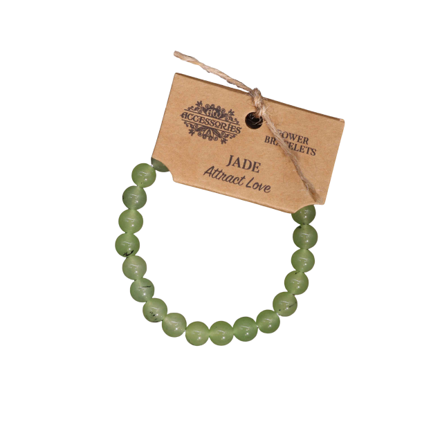 N�rbillede af et elastisk Jade Power Armb�nd set fra en skr� vinkel. De polerede gr�nne perler glimter i lyset, og m�rket med teksten 'JADE' og 'Attract Love' er tydeligt synligt mod den m�rke baggrund.