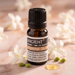 Et n�rbillede af en m�rk glasflaske med �terisk olie. Omkring flasken ligger friske, kridhvide jasminblomster, gr�nne vindruekerner og en smuk dr�be olie p� en glat, sart rosa overflade.