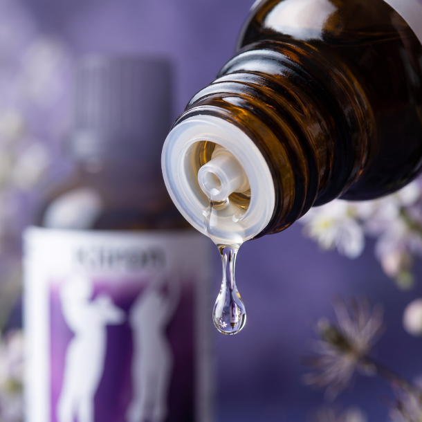 Et krystalklart makrobillede af en vanddr�be, der falder fra den indbyggede dr�bet�ller p� en m�rk ravfarvet glasflaske. Den bl�dt sl�rede baggrund kombinerer elegante, dybe violette og bl�de lilla nuancer med subtile hvide strejf, der symboliserer blomsterne fra Sort S�lvlys (Cimicifuga). Lyset er svalt, feminint og balancerende.