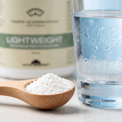 Et l�kkert n�rbillede af fint, snehvidt glucomannan pulver, der ligger perfekt afm�lt i en lys tr�m�leske. Ved siden af st�r et stort, dugv�dt glas rent vand. Billedet er lyst, klinisk og friskt.