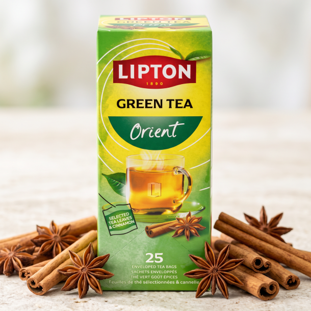 N�rbillede af den h�jformatede, lysegr�nne og gule Lipton Orient te�ske st�ende skarpt p� en lys stenoverflade. �gte kanelst�nger og hele stjerneanis ligger dekorativt spredt foran �sken i et bl�dt dagslys.