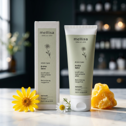 Mellisa Arnica Salve i salviegr�n tube og �ske anrettet p� lyst marmor, omgivet af gul arnica-blomst, kamille og gylden bivoks i et nordisk, eksklusivt milj�.