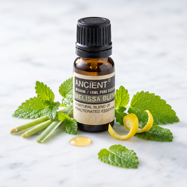 Et n�rbillede af en m�rk glasflaske med �terisk olie. Omkring flasken ligger der friske, savtakkede citronmelisse-blade, et strejf af citrongr�s og lyse citronskiver p� en lys, glat overflade.