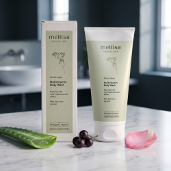 Mellisa kropsvask i salviegr�n tube og �ske anrettet p� lyst marmor, omgivet af acai-b�r, friskt aloe vera og rosenblade i et nordisk, eksklusivt bademilj�.