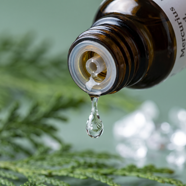 Et krystalklart makrobillede af en vanddr�be, der falder fra den indbyggede dr�bet�ller p� en m�rk ravfarvet glasflaske. Den bl�dt sl�rede baggrund kombinerer afd�mpede, salviegr�nne nuancer fra Thuja med krystallinske, hvide strejf af rent mineralsalt (Kaliumsulfat). Lyset er ekstremt rent, beroligende, k�ligt og udstr�ler absolut harmoni i halsen, strukturel lethed og hom�opatisk pr�cision.