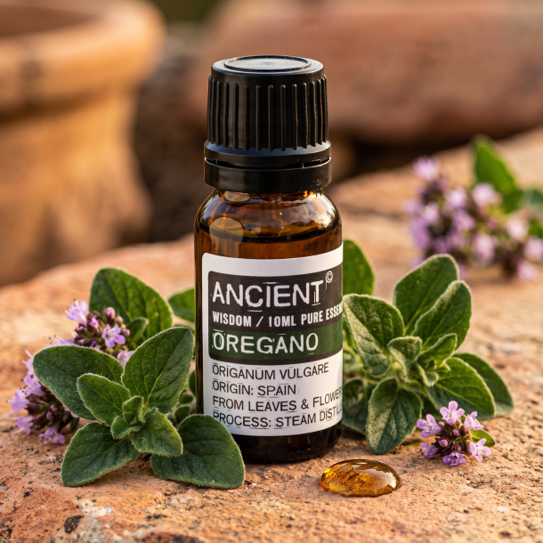 Et n�rbillede af en m�rk glasflaske med �terisk olie. Omkring flasken ligger friske, m�rkegr�nne oreganoblade og sm� lilla blomster badet i varmt middelhavslys p� en rustik flade.