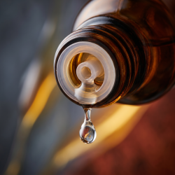 Et krystalklart makrobillede af en vanddr�be, der falder fra den indbyggede dr�bet�ller p� en m�rk ravfarvet glasflaske. Den bl�dt sl�rede baggrund kombinerer dybe, m�rke skifergr� nuancer fra bly (Plumbum) med varme, lysende, gyldne strejf af flydende honning og rustr�d skovmyre (Formica). Lyset er utroligt klart, bl�dg�rende og udstr�ler absolut indre varme, strukturel opl�sning og hom�opatisk pr�cision.