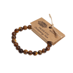 Tiger�je Power Armb�nd med naturlige 8mm krystalperler. Armb�ndet ligger fladt med et brunt kraftpapir-m�rke, der viser teksten 'AW ACCESSORIES POWER BRACELETS', 'TIGER EYE' og 'Overcoming Fear'.