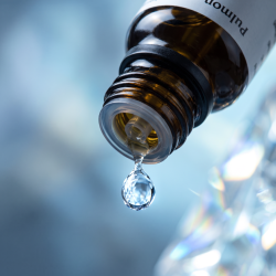 Et krystalklart makrobillede af en vanddr�be, der falder fra den indbyggede dr�bet�ller p� en m�rk ravfarvet glasflaske. Den bl�dt sl�rede baggrund kombinerer afk�lende, rene skiferbl� og luftige lysebl� nuancer med lyse glimt, der leder tankerne hen p� lys, fosfor og frisk luft. Lyset er ekstremt klart, udvidende og udstr�ler absolut flow, lethed i brystet og hom�opatisk pr�cision.