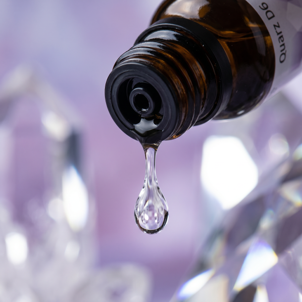 Et krystalklart makrobillede af en vanddr�be, der falder fra den indbyggede dr�bet�ller p� en 1:1 realistisk m�rk ravfarvet glasflaske. Den bl�dt sl�rede baggrund kombinerer sarte, k�lige lavendelnuancer med intense, krystallinske glimt af rent, hvidt lys og geometriske prisme-refleksioner (Quarz/Kisel). Lyset er ekstremt klart, opbyggende, og udstr�ler absolut strukturel formkraft, indre klarhed og hom�opatisk pr�cision.