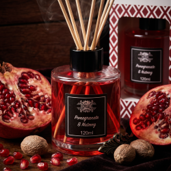 Et n�rbillede af en elegant glasflaske med duftpinde. Dyb rubinr�d v�ske i flasken omgivet af �bne, saftige granat�bler og hele muskatn�dder p� en m�rk baggrund.