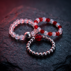 Et eksklusivt n�rbillede af tre 'Blood Moon' perleringe med rubin og m�nesten, smukt pr�senteret p� en m�rk, struktureret stenoverflade badet i et mystisk, dybr�dt m�neskin.
