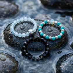 Et eksklusivt n�rbillede af tre 'Endless Ocean' perlerringe med akvamarin, turkis og obsidian, smukt pr�senteret p� en m�rk, v�d stenoverflade badet i et bl�dt og naturligt lys.