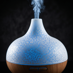 Et n�rbillede af overfladen p� en kuppelformet hvid aroma diffuser med et smukt krakeleret m�nster, hvor et roligt bl�t lys gl�der igennem spr�kkerne. En fin str�le af k�lig damp stiger op mod en m�rk baggrund.