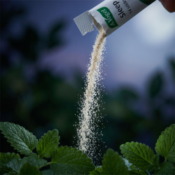 N�rbillede af et let, sandfarvet granulatpulver der h�ldes ud af en A. Vogel Sleep stick, med friske gr�nne urter i en bl�d og sl�ret aftenbaggrund.