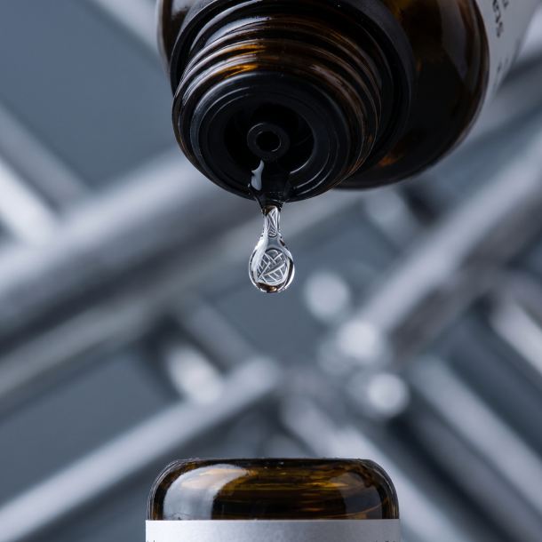 Et krystalklart makrobillede af en vanddr�be, der falder fra den indbyggede dr�bet�ller p� en 1:1 realistisk m�rk ravfarvet glasflaske. Den bl�dt sl�rede baggrund best�r af strukturerede, k�lige skifergr� og metalliske s�lvnuancer (Stannum/Tin), der afspejler faste, rytmiske linjer. Lyset er ekstremt klart, formgivende, og udstr�ler absolut strukturel arkitektur, indre kropslig form og hom�opatisk pr�cision.