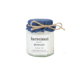 En klassisk glaskrukke med et bl�t stofl�g fyldt med ren hvid H�rvejssalt Sydesalt. En lille bunke saltkrystaller ligger ved siden af glasset.