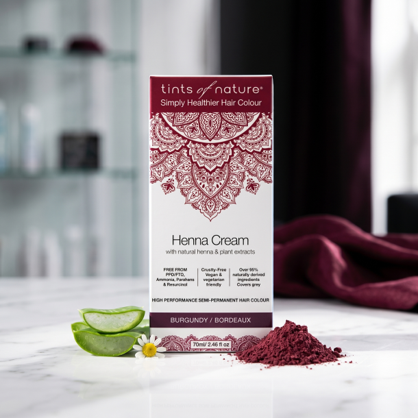 Tints of Nature Henna Burgundy �ske anrettet p� hvidt marmor, omgivet af frisk aloe vera, kamille og m�rk henna i et moderne, eksklusivt salon-milj�.