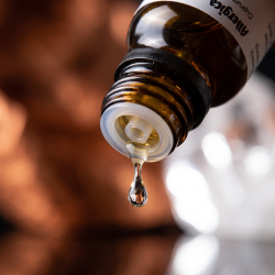 Et krystalklart makrobillede af en vanddr�be, der falder fra den indbyggede dr�bet�ller p� en m�rk ravfarvet glasflaske. Den bl�dt sl�rede baggrund kombinerer dybe, varme kobbernuancer (Cuprum) med skarpe, hvide, krystallinske glimt af ren kisel (Quartz). Lyset er utroligt fokuseret, groundende og udstr�ler absolut indre ro, afsp�nding og hom�opatisk pr�cision.