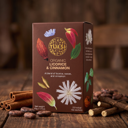 N�rbillede af den brune Tulsi te�ske st�ende p� et m�rkt, r�t tr�bord, omgivet af hele kanelst�nger, rustikke kakaob�nner og t�rret lakridsrod i et varmt, d�mpet lys.