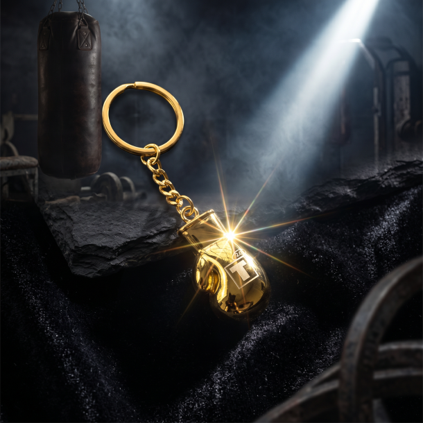 Skinnende guld Tyson 2.0 boksehandske n�glering liggende p� m�rk skifer i dramatisk belysning.