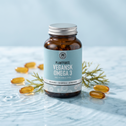 En sund og bevidst kvinde i et lyst hjem, der holder to gyldne veganske Omega-3 kapsler klar til indtagelse for at underst�tte hjertets og hjernens sundhed.