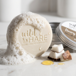 Et n�rbillede af en rigt skummende, lys shampoo bar omgivet af friske, hvide kokosn�dde-stykker og en gylden dr�be arganolie.