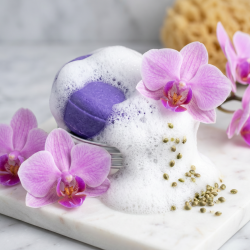 Et n�rbillede af en rigt skummende, intens lilla shampoo bar omgivet af friske, lyser�de orkid�blomster og sm�, gr�nne hampefr�.