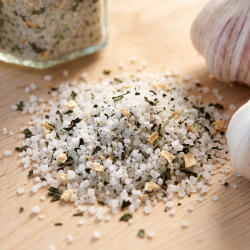 Makrobillede af hvide, sm�kornede saltkrystaller smukt blandet med m�rkegr�nne br�nden�ldeblade og sm� hvidl�gsstykker, badet i et lunt, indbydende lys p� et tr�br�t.