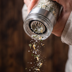 Makrobillede af en saltkv�rn i aktion, der drysser friske, sm�kornede saltkrystaller og t�rrede suppeurter ned i en varm suppe.