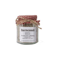 En smuk glaskrukke med et r�d- og hvidternet stofl�g fyldt med H�rvejssalt sydesalt blandet med br�nden�lde og hvidl�g. Et friskt hvidl�g og en gr�n br�nden�lde ligger ved siden af krukken.