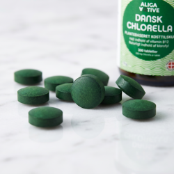 Et utroligt t�t n�rbillede af m�rkegr�nne, rene chlorella tabletter der ligger og reflekterer lyset p� et glat, hvidt marmorbord.