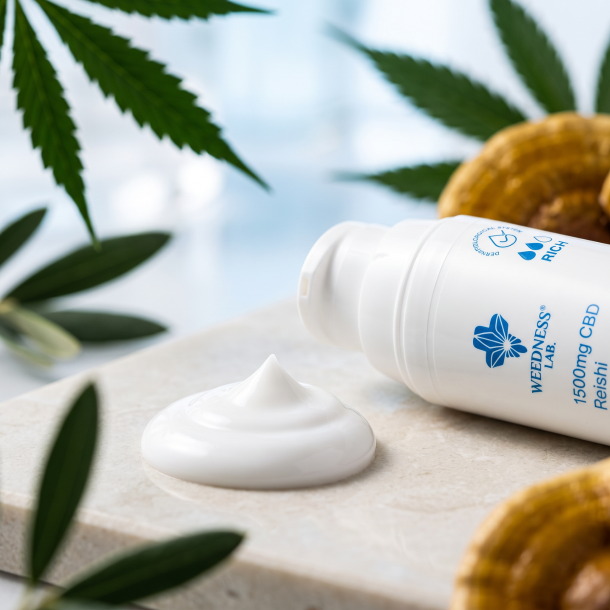 Hvid, rig barrierecreme p� en glat overflade ved siden af en Weedness CBD Cream flaske.