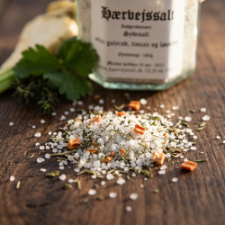 Makrobillede af kridhvide, sm�kornede saltkrystaller blandet med gr�nne og orange urtedrys, der ligger p� en rustik tr�overflade badet i varmt lys.